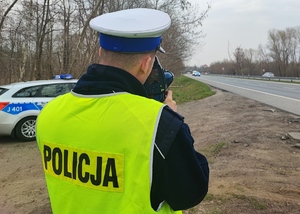 Policjant stoi przy drodze i kontroluje prędkość jadących samochodów