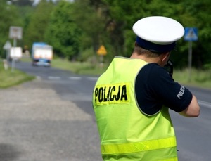 Policjant stoi przy drodze, kontroluje prędkość pojazdów