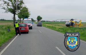 zdjęcie przedstawiające drogę, na drodze policjant i pojazdy, obok drogi na polu śmigłowiec
