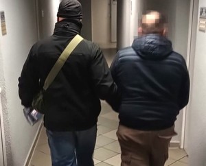 Nieumundurowany policjant prowadzi zatrzymanego korytarzem komendy