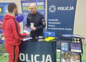Grafika przedstawia policyjne stoisko promocyjne oraz policjantów
