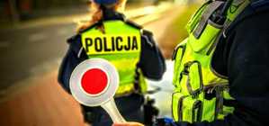 Grafika przedstawia tarczę do zatrzymywania pojazdów. W tle widać umundurowanego policjanta.