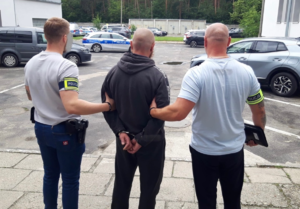 zdjęcie kolorowe - dwóch funkcjonariuszy prowadzą zatrzymanego mężczyznę