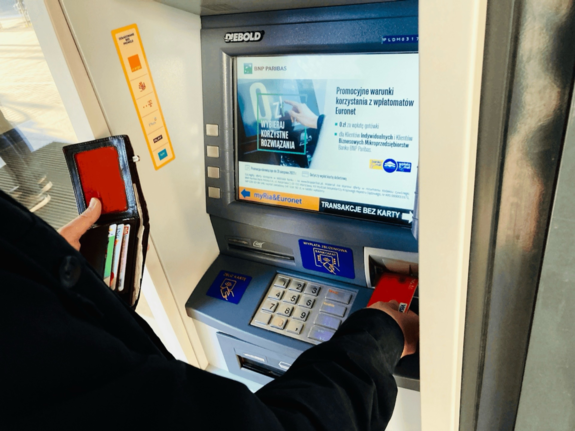 zdjęcie kolorowe: osoba wypłacająca pieniądze z bankomatu