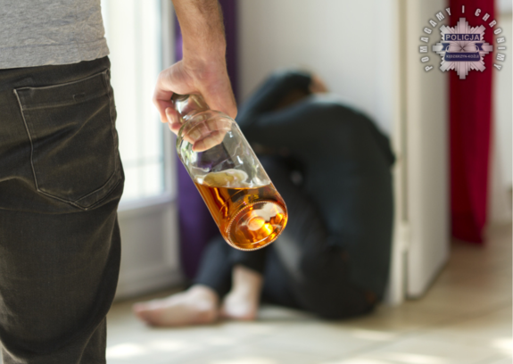 mężczyzna z butelką alkoholu a w tle skulona kobiet