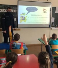 Policjant w klasie rozmawia z dziećmi o bezpieczeństwie wykorzystując prezentację multimedialną