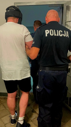 Zdjęcie przedstawia zatrzymanego mężczyznę w kasku, obok stoi policjant.