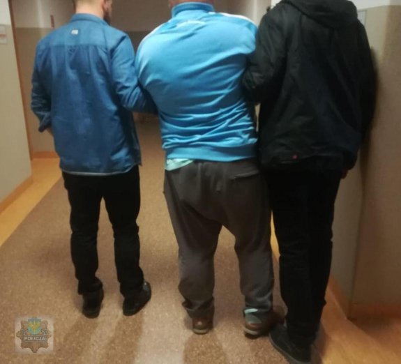dwaj policjanci pionu kryminalnego- nieumundurowani prowadzą zatrzymanego. Mężczyzna podejrzany jest o oszustwa.