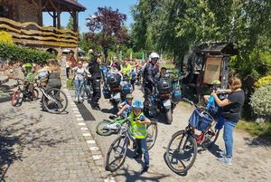 Miejsce zbiórki. Grupa dzieci z rowerkami i dwa policyjne motocykle. obok nich policjanci w kaskach.