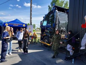 Zdjęcie w kolorze przedstawia młode osoby wychodzące z czarnej ciężarówki, po lewej stronie stoi policjantka.