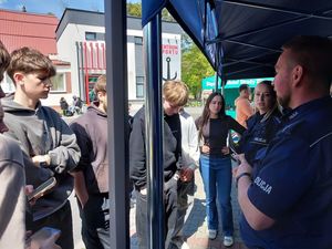 Zdjecie w kolorze przedstawia młodych meżczyzn, którzy rozmawiają z policjantem i policjantką. W tle budynek centrum sportu Kotwica.
