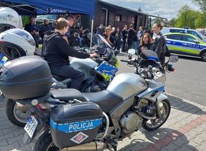 Zdjecie w kolorze przedstawia dwa motocykle policyjne na jednym z nich po lewej stronie siedzi młoda kobieta. W tle czarna ciezarówka po lewej oraz radiowóz po prawej stronie.