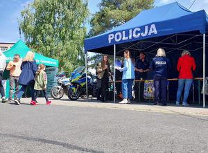 Zdjęcie w kolorze przedstawia stoisko ( namiot z napisem policja) po prawej stronie i po stronie lewej stoisko ( namiot z napisem straż graniczna). Przy stoiskach osoby zainteresowane.