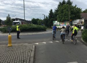 Zdjęcie w kolorze przedstawia rowerzystów jadących po jezdni, po lewej stronie policjant kierujący ruchem na rondzie.