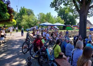 Zdjęcie w kolorze przedstawia grupę wielu osób na amfiteatrze w Gorzowie Ślaskim. W tle zaparkowane 2 policyjne pojazdy i stojący przy nich funkcjonariusze.