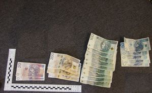 Zdjęcie w kolorze, przedstawia banknoty rozłożone na ciemnej tkaninie w nominałach kolejno od lewej strony 20 złotych , dwieście złotych, sto złotych i pięćdziesiąt złotych. W lewym dolnym rogu miara ze skalą.