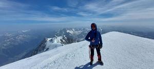 Alpinista na szczycie Mont Blanc. W tle ośnieżone szczyty Alp.