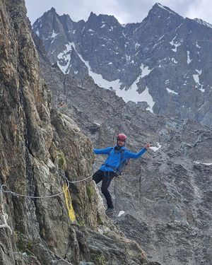 Skalne zbocze góry na nim alpinista trzymający się liny asekuracyjnej.