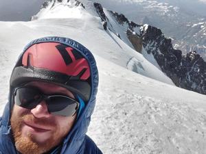 Zdjęcie selfie. Głowa alpinisty w kasku ochronnym i okularach na szczycie Mont Blanc. W tle ośnieżone Alpy.
