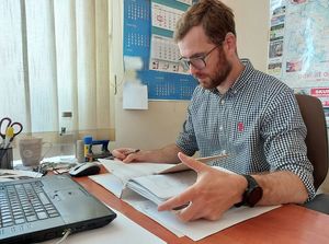 Pracownik Oleskiej komendy Policji siedzi za biurkiem i przegląda akta sprawy. Przed nim klawiatura laptopa.