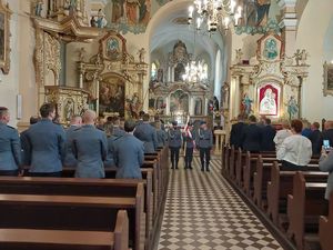 Zdjęcie w kolorze, przedstawia policjantów w umundurowaniu galowym od lewej stojącychw kościelnych ławkach, na wprost stoją trzej policjanci Pocztu sztandarowego Oleskiej Komendy, za nimi ołtarz w tle obraz Archanioła Michała.