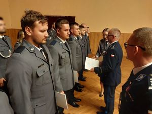 Zdjęcie w kolorze, przedstawia Policjantów w dwóch szeregach stojących po lewej stronie,obok  Zastępca Komendanta Wojewódzkiego insp. Krzysztof Buchała w asyście policjantki wręcza akty mianowania na wyższe stopnie policyjne, obok Komendant Powiatowy Policji w Oleśnie insp. Paweł Kolczyk.