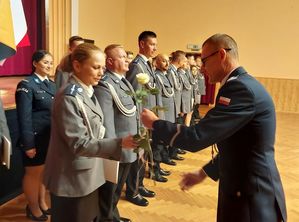 Zdjęcie w kolorze, przedstawia Policjantów w dwóch szeregach stojących po lewej stronie, na pierwszym planie Komendant Powiatowy Policji w Olesnie insp. Paweł Kolczyk wręcza biała różę policjantce.