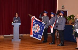 Zdjęcie w kolorze przedstawia po prawej stronie Poczet Sztandarowy Oleskiej Komendy dalej za mównicą stoi policjantka w tle bordowa zasłona.