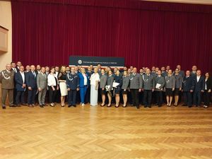 Zdjęcie w kolorze przedstawia wszystkich uczestników uroczystości pozujących do wspólnego zdjęcia na tle bordowej Zasłony.