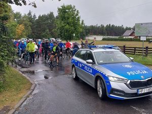 Zdjęcie w kolorze przedstawia na pierwszym planie radiowóz, tuz za nim peleton rowerzystów czekający na start.