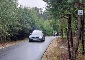 Zdjęcie w kolorze przedstawia  radiowóz na jezdni kilkanaście metrów  za nim uczestnicy rajdu na rowerach.