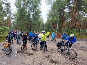 Zdjęcie w kolorze przedstawia uczestników rajdu z rowerami na  leśnym rozdrożu.