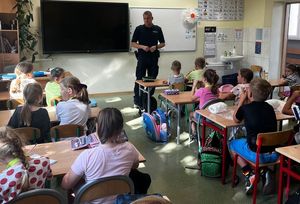 Zdjęcie w kolorze przedstawia policjanta stojącego na środku klasy, uczniowie siedzą w ławkach.
