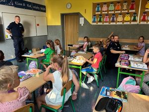 Zdjęcie w kolorze przedstawia policjanta stojącego na środku klasy, uczniowie siedzą w ławkach.