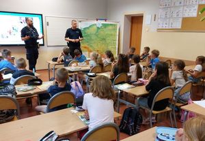Zdjęcie w kolorze przedstawia policjantów stojących w klasie , uczniowie siedzą w ławkach.
