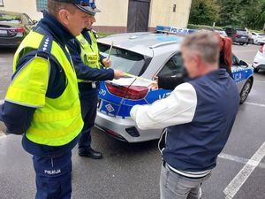 Zdjęcie w kolorze przedstawia jak policjanci wręczają mężczyźnie i kobiecie odblaski.