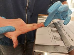 Zdjęcie w kolorze przedstawia młodzież podczas zajęć w pracowni technika kryminalistyki. Uczniowie sami wykonują odbitki palców.