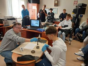 Zdjęcie w kolorze przedstawia młodzież podczas zajęć w pracowni technika kryminalistyki. Uczniowie sami wykonują odbitki palców.