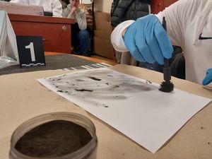 Zdjęcie w kolorze przedstawia młodzież podczas zajęć w pracowni technika kryminalistyki. Uczniowie sami ujawniają odbitki dłoni na kartce papieru.