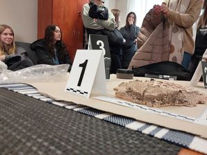 Zdjęcie w kolorze przedstawia stolik w pomieszczeniu technika kryminalistyki na którym są rozłożone znaczniki z numerami oraz rekwizyty, miedzy innymi gipsowy odcisk podeszwy.