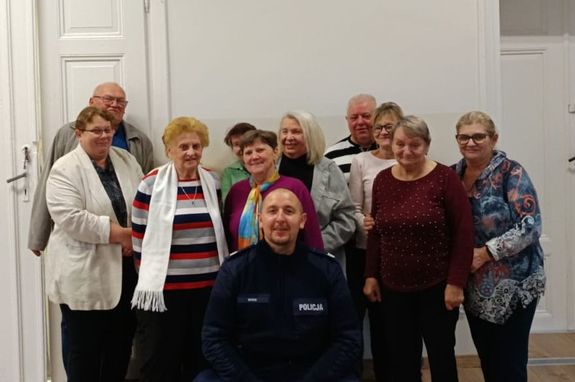 Zdjęcie w kolorze przedstawia grupę seniorów pozujących do zdjęcia z policjantem.