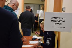 Zdjęcie w kolorze przedstawia stanowisko ewidencyjne przy którym siedzi policjantka obok pracownicy cywilni.