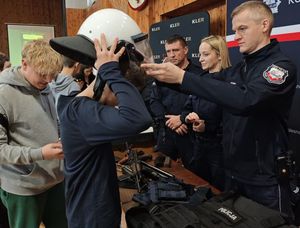 Zdjęcie w kolorze przedstawia stoisko policyjne z funkcjonariuszami, którzy promują służbę demonstrując uczniom jednostki broni i elementy wyposażenia.
