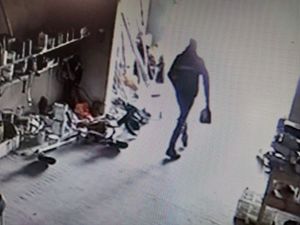 Zdjęcie w kolorze przedstawia kadr z zapisu monitoringu gdzie z magazynu z narzędziami wychodzi mężczyzna trzyma coś w prawej dłoni, obraz jest pozbawiony ostrości.