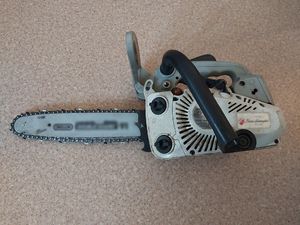 Zdjęcie w kolorze przedstawia piłę spalinową położona na podłodze.