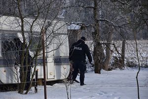 Zdjęcie w kolorze przedstawia dwóch policjantów sprawdzających przyczepę kempingową w zaśnieżonym otoczeniu.