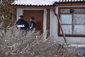 Zdjęcie w kolorze przedstawia policjantów przed drzwiami altany działkowej w zimowej scenerii.