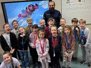 Zdjęcie w kolorze, przedstawia grupę uczniów pozujących do zdjęcia z policjantem, za nimi na ekranie slajd z dziećmi podczas zabawy na śniegu.