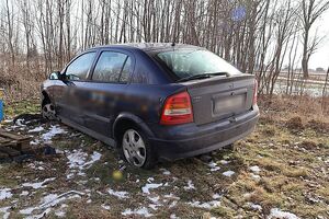 Zdjęcie w kolorze przedstawia granatowego opla zaparkowanego na obszarze rolniczym w tle zarośla.