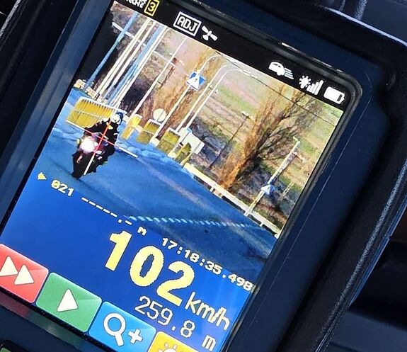 Zdjęcie w kolorze przedstawia ekran miernika prędkości z wizerunkiem motocyklisty na jezdni w dolnym prawym rogu prędkość 102 km/h